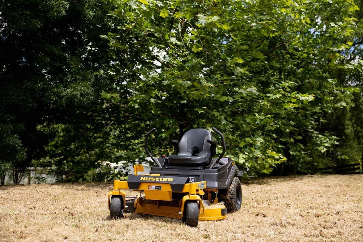 Zero-turn ride-on mower on a cut block beneath deciduous trees at the end of a seasonal clean up